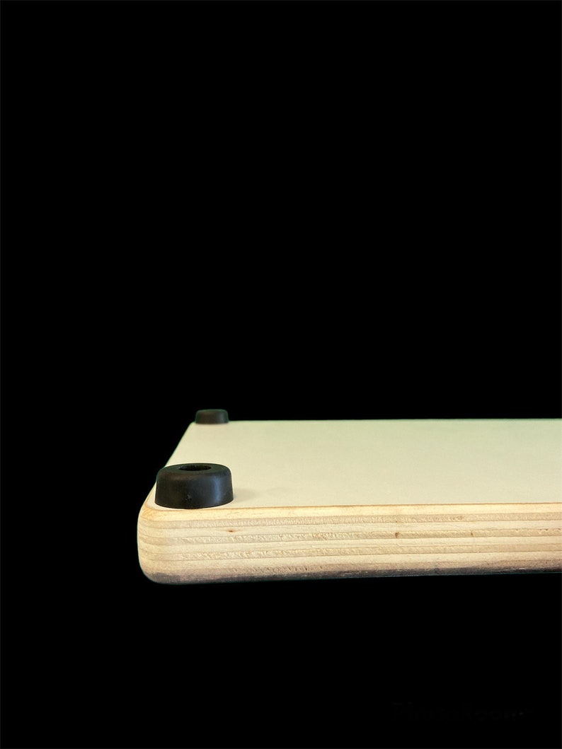 May include: A close-up of the bottom edge of a light wood cutting board with black rubber feet.