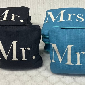 May include: Two sets of bean bags, one set in black with white "Mr." lettering and one set in blue with white "Mrs." lettering.
