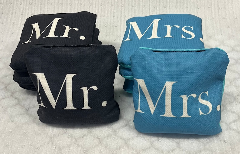 May include: Two sets of bean bags, one set in black with white "Mr." lettering and one set in blue with white "Mrs." lettering.