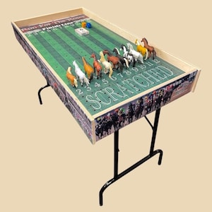 May include: A wooden horse racing game with a green track and colorful horses. The game is set up on a folding table with black legs. The game includes dice and a finish line.