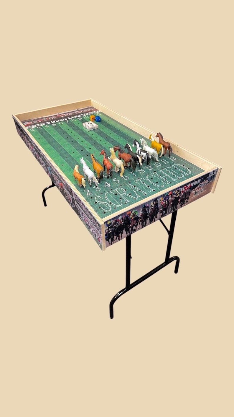 May include: A wooden horse racing game with a green track and colorful horses. The game is set up on a folding table with black legs. The game includes dice and a finish line.