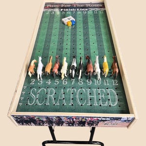 May include: A wooden game board with a green felt playing surface and a horse racing theme. The board has a finish line, numbered spaces, and a 'SCRATCHED' area. There are 12 plastic horses on the board, and two dice are in the center of the board.