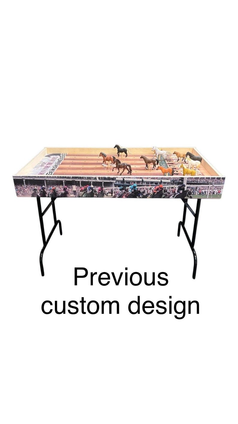May include: A wooden horse racing game table with a black metal frame. The table top features a colorful racetrack design with a crowd of people watching the race. There are several plastic horses on the track.