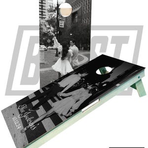 May include: A black and white photo of a couple walking on a crosswalk. The photo is on a wooden cornhole board with the text "The Jacksons" and "10.12.24" printed on it. The board is green and has a white trim.