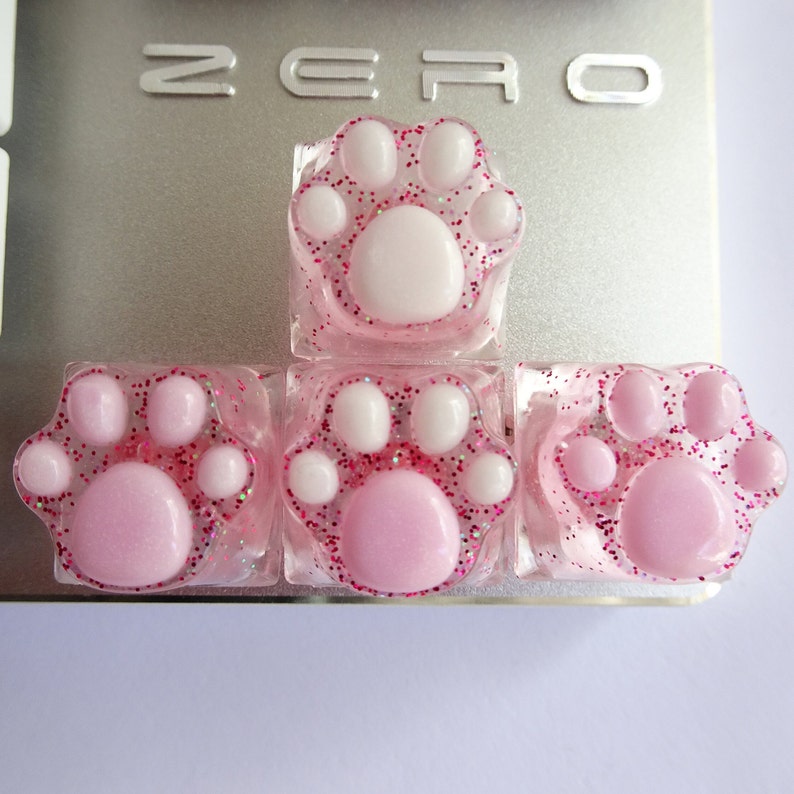 Four pink and white paw print keycaps with pink glitter.
