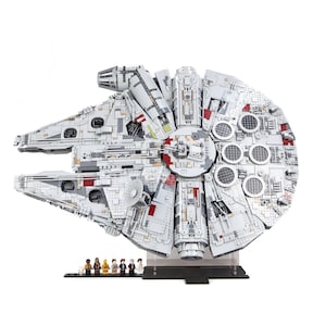 May include: A detailed model of the Millennium Falcon spaceship, primarily white with gray and red accents. The model includes intricate detailing and is displayed on a clear stand. Small character figures are lined up in front of the model.