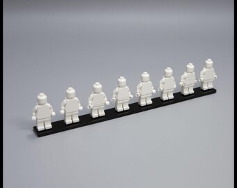 以下が含まれることがあります： 黒いベースの上に並んだ8体の白いレゴフィギュア。フィギュアは均等に配置され、クラシックなレゴミニフィギュアのデザインです。背景は無地のグレーです。