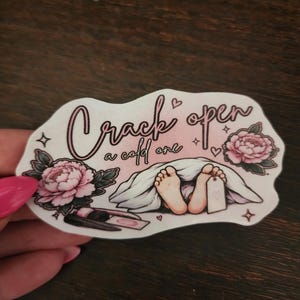 Puede incluir: Una pegatina troquelada con fondo degradado rosa que presenta el texto "Crack open a cold one" en letra negra. La ilustración muestra un par de pies bajo una sábana blanca con una etiqueta en el dedo, flanqueada por dos peonías rosas y brochas.
