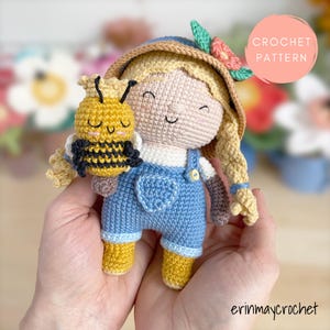 Könnte beinhalten: Häkelanleitung für eine süße Amigurumi-Puppe mit Latzhose und Strohhut, die eine gehäkelte Biene hält. Die Puppe hat blonde Haare und einen süßen Gesichtsausdruck.