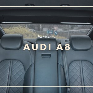 May include: Interior shot of the backseat of an Audi A8. The seats are black leather with a diamond pattern. The text "backseat" and "AUDI A8" are displayed in a white font.