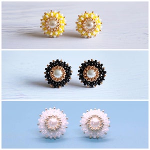 Peut inclure: Trois paires de boucles d'oreilles en perles avec un centre de perle. La première paire est jaune et blanche, la deuxième paire est noire et dorée, et la troisième paire est blanche et argentée.