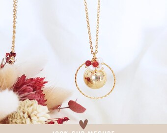 May include: A gold-colored necklace with a round pendant and a delicate chain. The pendant features a sphere within a circular frame, adorned with red and white beads. The text "100% SUR MESURE entièrement personnalisable" is at the bottom.