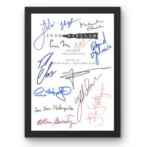 May include: A framed print featuring the title "Interstellar" with multiple signatures in various colors. The signatures are arranged around the title and credits, including "Directed by Christopher Nolan" and "Written by Nathan Nolan & Christopher Nolan."