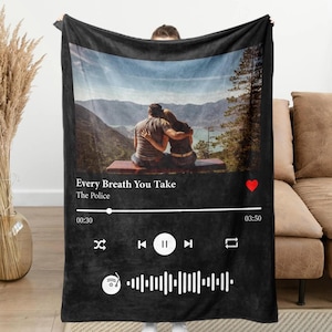 May include: Black fleece blanket featuring a photograph of a couple seated on a bench overlooking a mountainous landscape. The blanket incorporates a Spotify-inspired music player design, displaying the song "Every Breath You Take" by The Police.