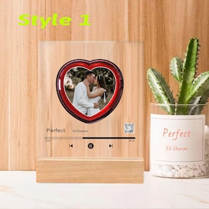 May include: A wooden photo frame with a red heart-shaped glass insert. The glass insert contains a photo of a couple kissing. The frame has a music player interface with the song "Perfect" by Ed Sheeran playing.
