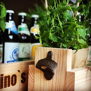 May include: A wooden crate with a bottle opener attached to the side. The crate is filled with potted plants and several glass bottles. The crate is labeled "lino's".