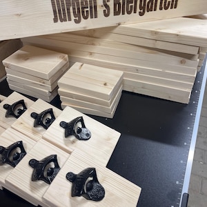 May include: A wooden sign with the text "J&uuml;rgen's Biergarten" engraved on it.  The sign is surrounded by stacks of wooden boards and bottle openers.