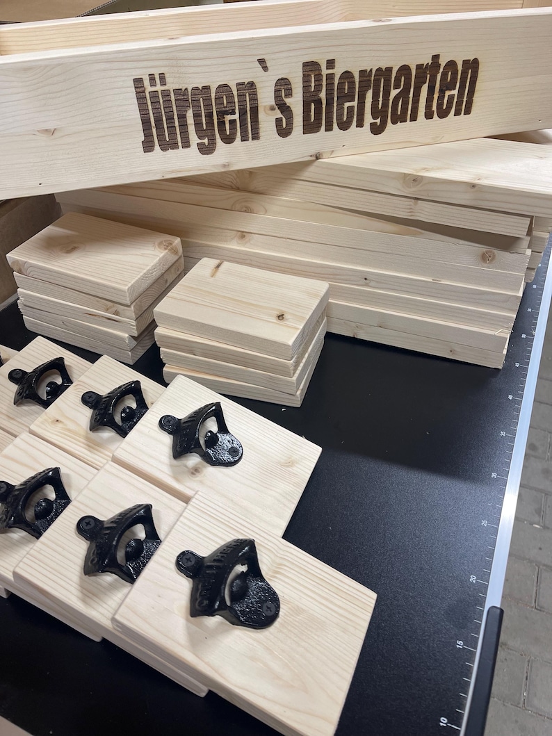 May include: A wooden sign with the text "J&uuml;rgen's Biergarten" engraved on it.  The sign is surrounded by stacks of wooden boards and bottle openers.