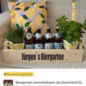 May include: A wooden crate with the text "J&uuml;rgen's Biergarten" on the front. The crate is filled with four bottles of beer, two potted plants, and a lemon-patterned pillow. Two wooden poles with the number "60" on them are in the background.