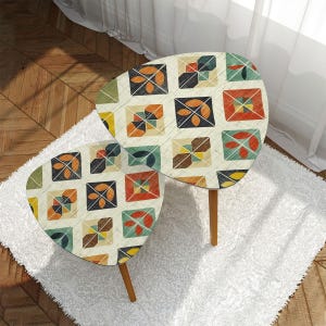 May include: Two nesting tables with a mid-century modern design. The tables have a cream-colored surface with a repeating pattern of colorful squares. The legs are made of wood. The tables are placed on a white rug.