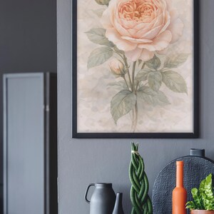 Pu&ograve; includere: Una stampa artistica da parete incorniciata raffigurante un'illustrazione ad acquerello di una grande rosa color pesca pallido in piena fioritura, accompagnata da due boccioli e foglie verdi su uno sfondo neutro e maculato.