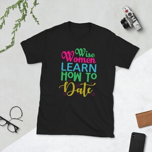 Può includere: Maglietta nera con il testo "Wise Women Learn How To Date" in lettere colorate con cuori rosa.