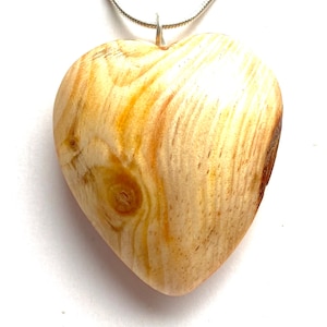 Puede incluir: Un colgante de corazón de madera con un patrón de veta de madera natural y una cadena de plata.
