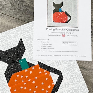 Könnte beinhalten: Ein Quilt-Block mit einer schwarzen Katze und einem orangefarbenen Kürbis mit weißen Sternen. Der unfertige Block misst 31,75 cm x 31,75 cm. Das dazugehörige Papier trägt die Aufschrift "Purring Pumpkin Quilt Block" von Kelly Lund.