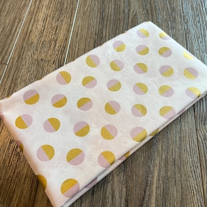 May include: Folded fabric with a pattern of pink and gold half-circles on a white background. The fabric is folded and appears to be a cotton or linen material. The gold has a slight shimmer.