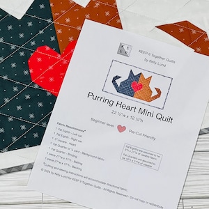 May include: A white sheet of paper with instructions for a "Purring Heart Mini Quilt" that measures 57 cm wide by 32 cm high. The instructions are for a beginner level quilter and are pre-cut friendly. The paper also includes a list of fabric requirements, including fat eighths, fat quarters, and a 1/2 yard of background fabric.