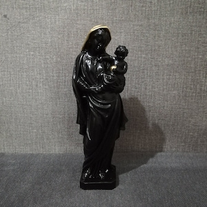 Può includere: Statua nera della Vergine Maria che tiene in braccio un bambino Gesù. La statua è realizzata in un materiale liscio e opaco e ha un bordo dorato sulla testa della Vergine Maria.