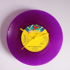 Puede incluir: Un reloj de vinilo morado con manecillas amarillas. La etiqueta central es amarilla con el texto "Jet Records" y "Sweet Talkin' Woman". Un artículo decorativo único.