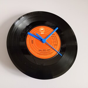Puede incluir: Un reloj de vinilo negro con agujas azules. La etiqueta del disco es naranja y presenta el texto "ABBA" y "MONEY, MONEY, MONEY". La etiqueta también incluye el texto "Epic" y "EPC 4713".