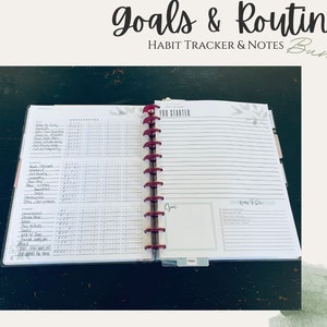 May include: An open planner with a red binding and a white cover. The planner has a habit tracker on the left page and a "Goals & Routines" section on the right page. The planner is labelled "Habit Tracker & Notes Bundle".