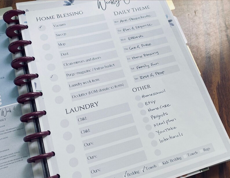 May include: A weekly planner page with a light gray background and a white grid. The page is divided into sections for "Home Blessing", "Laundry", "Daily Theme", and "Other". Each section has a list of tasks or activities to be completed. The page also includes checkboxes for each task.
