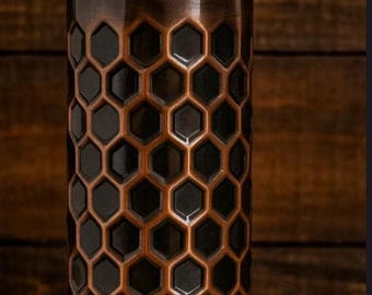 May include: A cylindrical copper water bottle featuring a dark, embossed honeycomb pattern across its body. The bottle has a smooth, rounded neck and a matching dark copper cap that sits securely on top, creating a uniform metallic appearance.