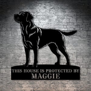 May include: Black metal sign featuring a Labrador Retriever silhouette. The sign reads "THIS HOUSE IS PROTECTED BY MAGGIE" in a distressed font. The dog is standing, facing left, with its head up. The sign is mounted on a brick wall.
