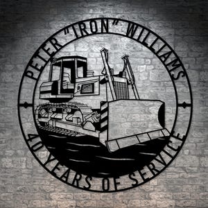Könnte beinhalten: Schwarzes Metallschild mit einer Bulldozer-Silhouette und dem Text "Peter "Iron" Williams 40 Years of Service".
