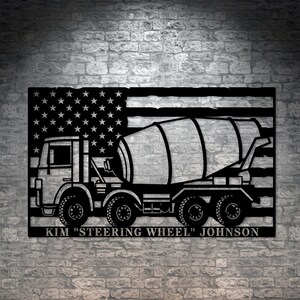 May include: Black metal silhouette of a cement mixer truck in front of an American flag with the text "KIM "STEERING WHEEL" JOHNSON" below.