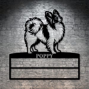 Könnte beinhalten: Schwarz-weiße Metall-Wandkunst eines Chihuahua-Hundes. Der Hund steht auf einem rechteckigen Schild mit dem Namen "POPPY". Der Hintergrund ist eine Backsteinmauer.