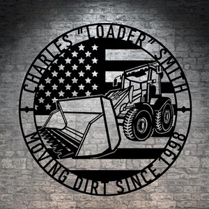 May include: Black metal wall art featuring a loader with an American flag design. The circular design includes the text "CHARLES 'LOADER' SMITH MOVING DIRT SINCE 1998". The loader is depicted in detail, with its bucket and wheels visible.