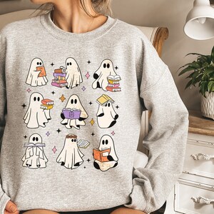 May include: A grey sweatshirt featuring a design of several ghosts reading books. The ghosts are white with black outlines and are holding stacks of colourful books.
