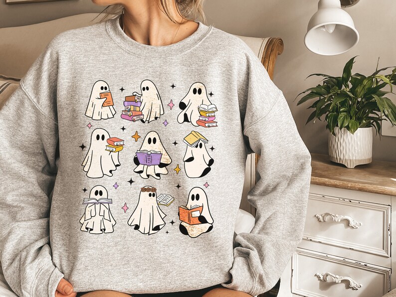May include: A grey sweatshirt featuring a design of several ghosts reading books. The ghosts are white with black outlines and are holding stacks of colourful books.