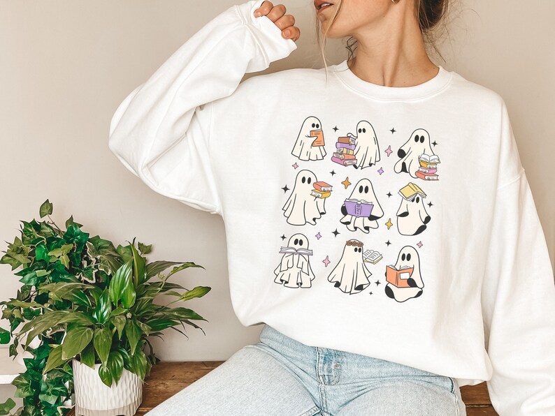 May include: White sweatshirt featuring a design of several ghosts reading books. The ghosts are in different positions and have books of various colours.