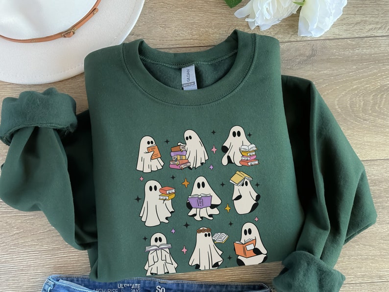 May include: A dark green sweatshirt featuring a design of several white ghosts reading books. The ghosts are depicted in different poses, some holding books, others with books on their heads. The sweatshirt has a crew neck and long sleeves.