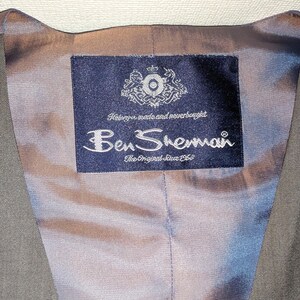 May include: Close-up of the inside of a grey waistcoat. The lining is a pale blue-grey colour. A navy blue label with the Ben Sherman logo and text is sewn into the lining. The label also includes the text "The Original Since 1963."