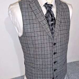 May include: A gray plaid vest with black buttons, worn over a white dress shirt and a patterned tie. The vest features a classic, tailored design with a subtle checkered pattern.