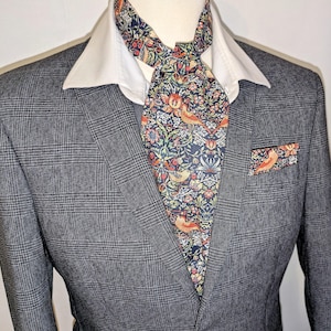 Peut inclure: Un blazer à carreaux gris avec une chemise à col blanc, une cravate ascot à motifs et une pochette assortie. La cravate ascot et la pochette présentent un fond bleu marine avec un motif floral et d'oiseaux orange, rouge et vert.