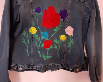 以下が含まれることがあります： 背面にカラフルな刺繍のバラが施された青いデニムジャケット。バラは赤、黄、ピンク、青、紫です。