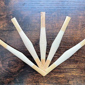 May include: Five natural bamboo reeds arranged in a fan shape on a brown wooden surface. The reeds are light brown with a white tip.